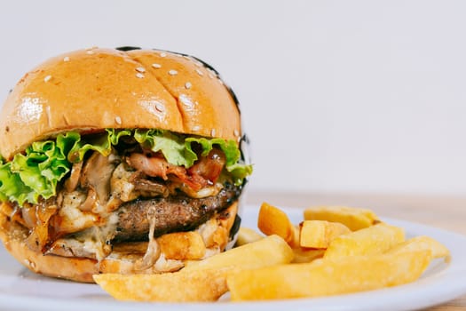 Big cheeseburger with fries served with copy space. Homemade burger with french fries on a plate on wooden table