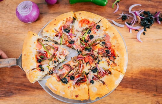 Top view of spatula taking a slice of supreme pizza with vegetables. Spatula taking a slice of supreme pizza with spatula, High angle view