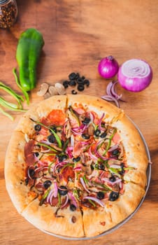 Top view of supreme pizza with olives and vegetables on wooden table. Delicious supreme pizza with vegetables on wooden background