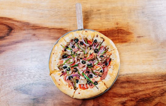 Top view of supreme pizza with olives on the wooden table. High angle view of supreme pizza with olives on wooden background