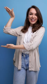 Charming brunette 30 year old female person dressed in a shirt and jeans shows her hand at an advertising offer.