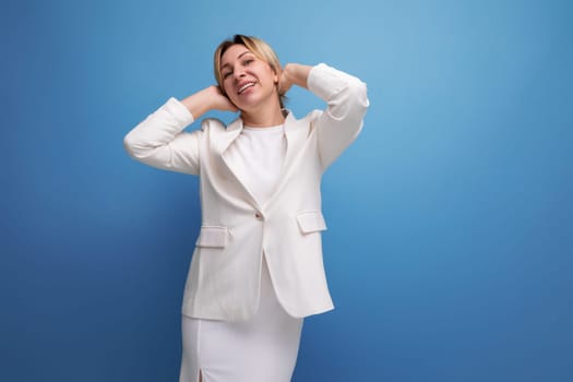 well-groomed slim young blond career woman in a white elegant jacket and skirt on a blue background with copy space.