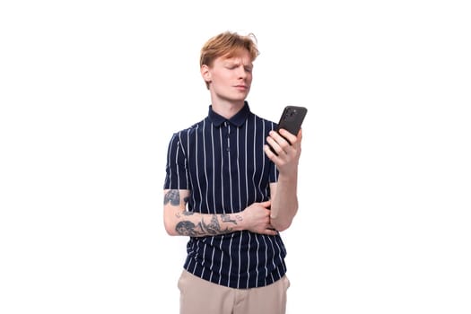 25s blond man dressed in a T-shirt with tattoos sits on the phone.