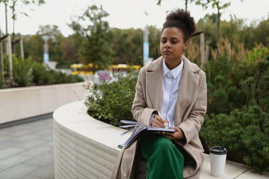 american young woman designer writes plan while sitting outdoors in spring.