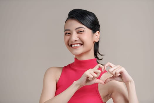 Pretty romantic young asian woman making a heart gesture with her fingers in front of her chest 