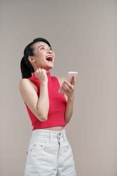 Pretty young asian woman using smartphone standing on isolated white background feeling happy.
