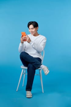 Portrait of smiling young man using smartphone sitting on chair 