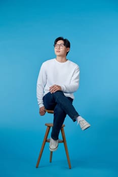 Portrait of smiling happy man sits on the stool isolated on blue.