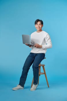 Full length of attractive man office worker sit stool use netbook conference on blue background