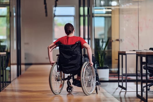 A modern young businesswoman in a wheelchair is surrounded by an inclusive workspace with glass-walled offices, embodying determination and innovation in the business world.