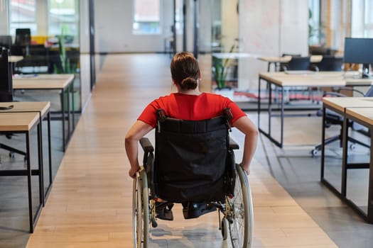 A modern young businesswoman in a wheelchair is surrounded by an inclusive workspace with glass-walled offices, embodying determination and innovation in the business world.