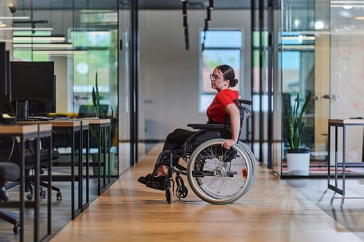 A modern young businesswoman in a wheelchair is surrounded by an inclusive workspace with glass-walled offices, embodying determination and innovation in the business world.