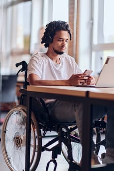 An African American businessman in a wheelchair takes a work break, using his smartphone while seated in a modern business startup coworking center, reflecting both inclusion and technology integration