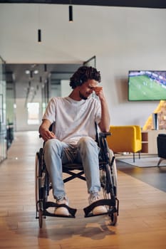 A sad businessman in a wheelchair occupies a hallway within a modern startup coworking center, embodying inclusivity and determination in the business environment.