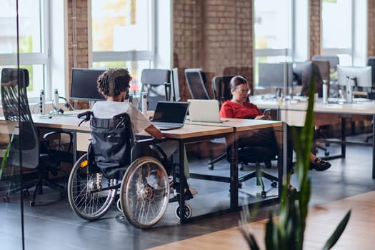 Business colleagues work within a modern startup coworking office, with one of them, an African America in a wheelchair, actively engaging with computers and laptops to collaboratively address various business challenges