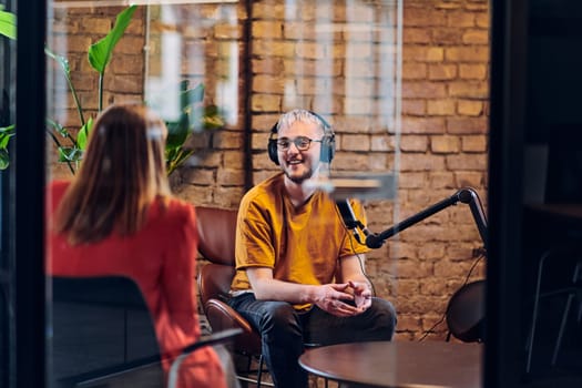 A gathering of young business professionals, some seated in a glass-walled office, engage in a lively conversation and record an online podcast, embodying modern collaboration and dynamic interaction.