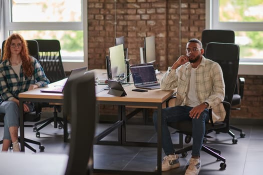 Group of colleagues, a woman with vibrant orange hair and a young African American businessman, sitting in a modern office space, symbolizing diverse collaboration and a dynamic work environment