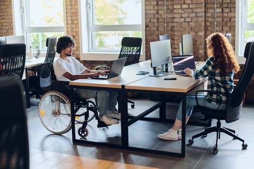 Business colleagues work within a modern startup coworking office, with one of them, an African America in a wheelchair, actively engaging with computers and laptops to collaboratively address various business challenges