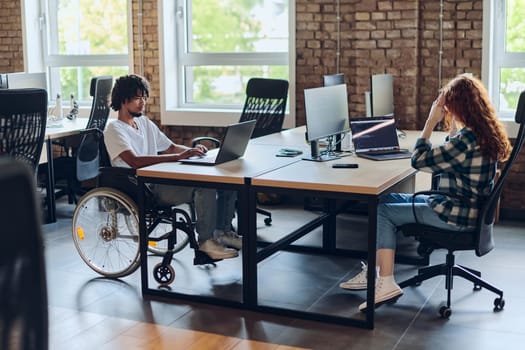 Business colleagues work within a modern startup coworking office, with one of them, an African America in a wheelchair, actively engaging with computers and laptops to collaboratively address various business challenges