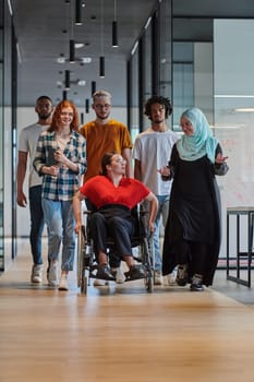 A diverse group of young business people walking a corridor in the glass-enclosed office of a modern startup, including a person in a wheelchair and a woman wearing a hijab, showing a dynamic mix of innovation and unity