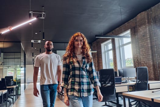 A woman with modern orange hair and an African American businessman walking together through the hallway of a contemporary coworking startup office, reflecting diversity and collaboration.