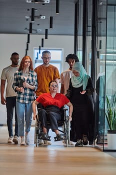 A diverse group of young business people walking a corridor in the glass-enclosed office of a modern startup, including a person in a wheelchair and a woman wearing a hijab, showing a dynamic mix of innovation and unity