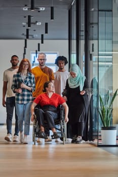 A diverse group of young business people walking a corridor in the glass-enclosed office of a modern startup, including a person in a wheelchair and a woman wearing a hijab, showing a dynamic mix of innovation and unity