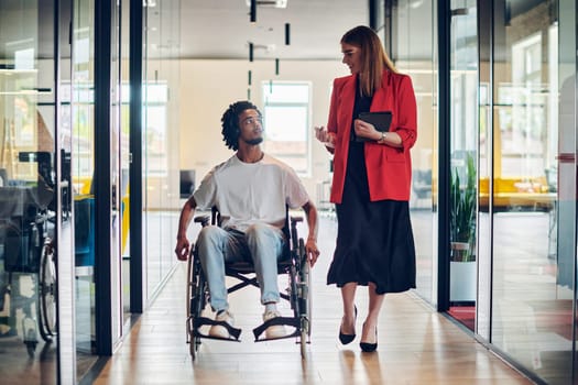 A group of young business people in a modern glass-walled office captures the essence of diversity and collaboration, while two colleagues, including an African American businessman in a wheelchair, reflect inclusivity and discuss solving business problems.