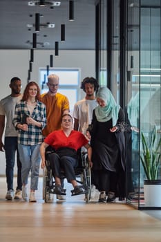 A diverse group of young business people walking a corridor in the glass-enclosed office of a modern startup, including a person in a wheelchair and a woman wearing a hijab, showing a dynamic mix of innovation and unity