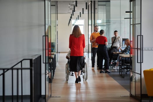 A group of young business people in a modern glass-walled office captures the essence of diversity and collaboration, while two colleagues, including an African American businessman in a wheelchair, reflect inclusivity and discuss solving business problems.