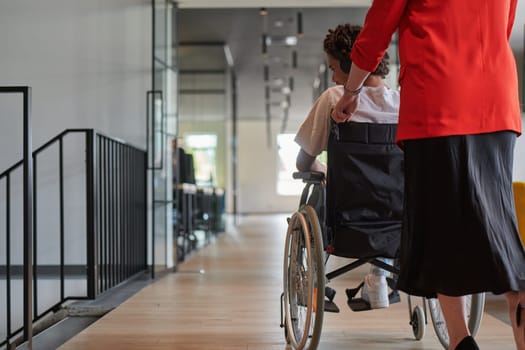 A group of young business people in a modern glass-walled office captures the essence of diversity and collaboration, while two colleagues, including an African American businessman in a wheelchair, reflect inclusivity and discuss solving business problems.