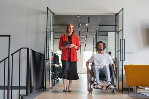 A group of young business people in a modern glass-walled office captures the essence of diversity and collaboration, while two colleagues, including an African American businessman in a wheelchair, reflect inclusivity and discuss solving business problems.