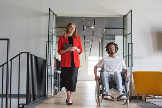 A group of young business people in a modern glass-walled office captures the essence of diversity and collaboration, while two colleagues, including an African American businessman in a wheelchair, reflect inclusivity and discuss solving business problems.