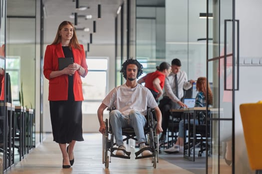 A group of young business people in a modern glass-walled office captures the essence of diversity and collaboration, while two colleagues, including an African American businessman in a wheelchair, reflect inclusivity and discuss solving business problems.