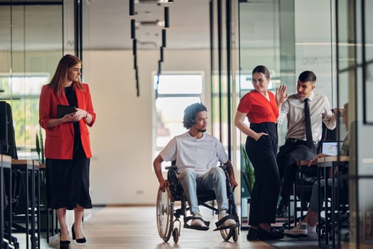 A group of young business people in a modern glass-walled office captures the essence of diversity and collaboration, while two colleagues, including an African American businessman in a wheelchair, reflect inclusivity and discuss solving business problems.