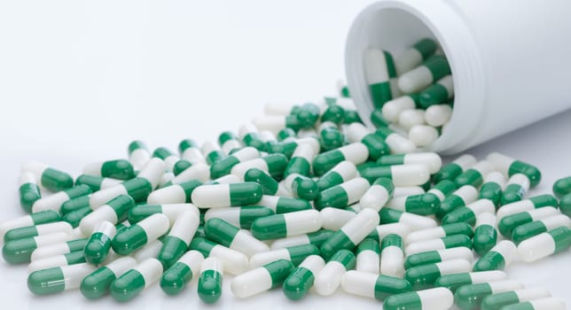 Green and white capsule pills spilled out of a white plastic bottle. Pharmaceutical industry. Prescription drug. Healthcare and medicine. Pharmacy product. Pharmaceutics. Capsule pill manufacture.