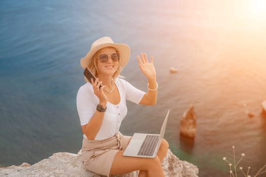 Freelance women sea working on the computer. Good looking middle aged woman typing on a laptop keyboard outdoors with a beautiful sea view. The concept of remote work