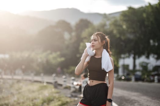 Portrait Young beautiful Asian woman wiping sweat after evening jogging in the park..