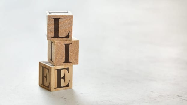 Pile with three wooden cubes - word LIE on them, space for more text / images at right side.