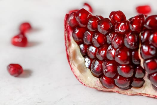 Closeup - red pomegranate gem like seeds, some fruits scattered on white board in background.