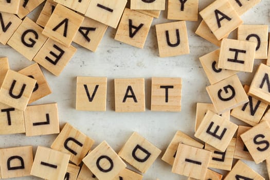 Top down view, pile of square wooden blocks with letters VAT (stands for Value added tax) on white board. 