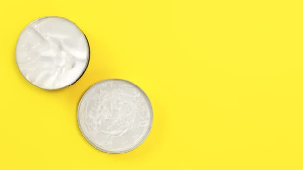 Tabletop view, metal round tin container with white cosmetic cream on yellow board, cap next to base, space for text right.