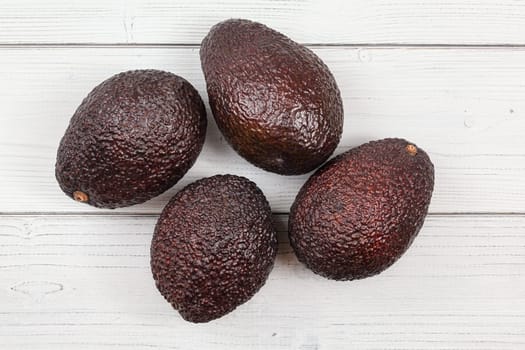 Tabletop view, four dark brown ripe avocados ( bilse cultivar ) on white boards desk.