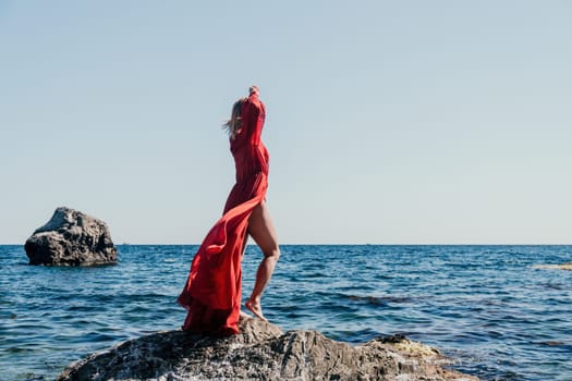 Woman travel sea. Young Happy woman in a long red dress posing on a beach near the sea on background of volcanic rocks, like in Iceland, sharing travel adventure journey