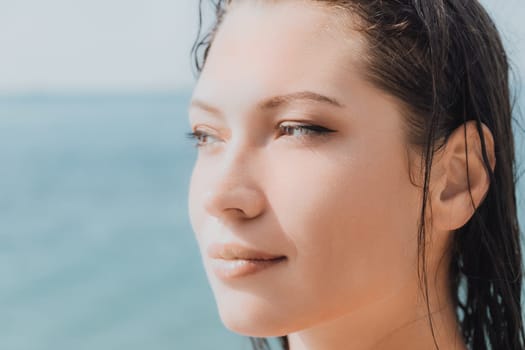 Close up shot of beautiful young caucasian woman with black hair and freckles looking at camera and smiling. Cute woman portrait in a pink bikini posing on a volcanic rock high above the sea