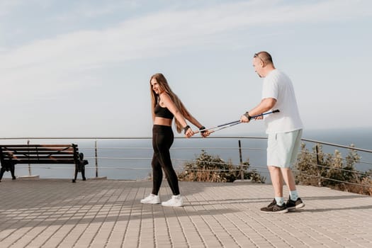 Happy Middle aged couple or friends practicing nordic walking in park near sea. Mature couple with trekking poles walking, practicing Nordic walking outdoors. Aging youthfully and sport concept.