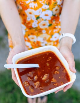 Bograch, borscht, thick spicy soup with beets and meat, close-up. The girl holds borscht in a plate, top view