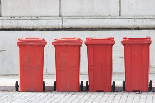 Red trash cans stand in a row on the street. Mid shot