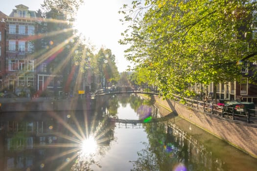 Netherlands. Sunny morning on the Amsterdam Canal. The bright sun is reflected in the water. House facades and footbridge