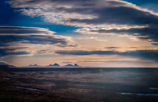 The sun is shining through the clouds over the mountains. Photo of the sun peeking through the clouds over the majestic mountains of Iceland